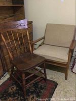 Two wooden chairs side by side: one spindle-back with carved top rail and one mid century modern style armchair with beige cushions.