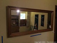 Full view of the large rectangular wall mirror mounted on a wall reflecting room elements such as window and furniture.