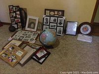 Photo showing multiple picture frames arranged on the floor, a globe on a stand, a decorative gourd, and the US Marine wall clock leaning against the wall