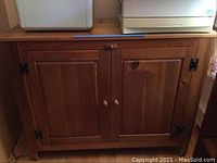 Closed view of the wooden cabinet, showing two doors with wooden knobs and metal hinges.