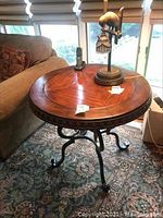 Full view of round wooden top table with ornate cast iron legs and brass elements, positioned near a sofa and window.