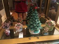 Full lot showing green ceramic Christmas tree, glass ball on stand, ceramic canister, and ceramic flower vases on glass table with mirror background.