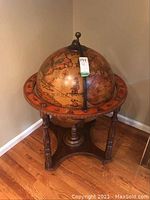 Globe shaped bar cabinet with antique map decoration and wooden carved base.