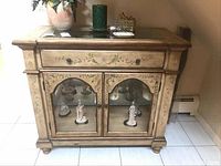 Front view of the wooden entrance showcase cabinet showing floral designs, black glass top, drawer, and glass doors with figurines inside.