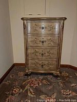 Front view of decorative chest of drawers with floral painted drawers and carved legs.