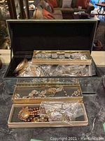 Jewelry box lid open showing three clear-lidded trays branded ‘Celebrity’ with necklaces and earrings