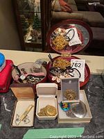 Top down view of jewelry box interior showing assorted costume jewelry including chain necklaces, a pendant, wristwatches with black and pink leather bands, and various rings and bracelets.