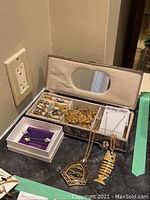 Open silver-tone jewelry box showing interior mirror and assortment of rings and chains