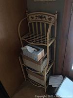 Full view of mini baker's rack in corner with some tissue boxes stored on shelves.
