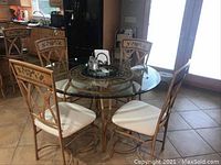 Full view of round glass top table with four matching chairs in kitchen setting, showing table base and chair cushions.