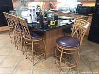 Five wooden bar stools arranged along a kitchen island, showing the grapevine motif on backrests and burgundy cushioned seats.