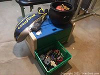 Photo showing blue-lid Little Tykes toy chest with beige and green base, Goodyear inflatable blimp on top, black cauldron holding fall decorations, and green bin with toys in front.