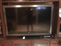 Full frontal view of the Sony Bravia TV on a wooden stand with remote controls placed on the stand.