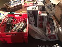 Assortment of Hess Trucks and original boxes seen in a red plastic container and on surface nearby.