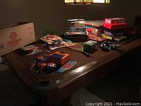 Wide shot of table with various board games, toys, books, and CDs in basement setting.