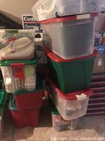 Multiple stacked plastic storage bins with red and green lids, partially translucent showing some Christmas items inside.