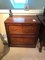 Front view of wooden file cabinet with two drawers and brass handles. Top drawer sticky.