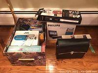Overall view of lot showing JVC and Canon camera boxes, Philips DVD player, and a leather case
