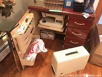 Full view of Singer Athena 1200 sewing machine on a wooden console with attached racks holding thread and sewing supplies. Portable carry case is placed on the floor.
