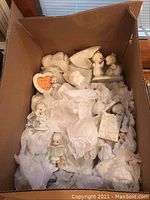 Box with multiple Precious Moments porcelain figurines wrapped in tissue paper showing figurines in various poses and one heart-shaped photo frame.