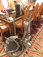 Kirby Ultimate G upright vacuum and accessories near dining chairs on patterned carpet
