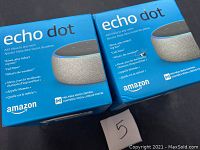 Two Amazon Echo Dot devices in blue retail boxes, showing front of packaging with product branding and features described.