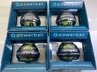 Four Powerball gyroscopic exercisers in original blue packaging, showing clear domes and internal gyroscopes.