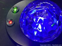Close-up of the projector showing the faceted dome light component illuminated in blue, along with red and green indicator lights on black base.