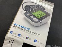 Photo of the product box showing the arm blood pressure monitor with features listed such as arrhythmia checking and tricolor backlight.