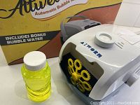 Bubble machine alongside small bottle of yellow bubble solution and product box