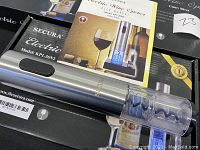 Two Secura electric wine openers in stainless steel finish shown on black Secura branded boxes with user manuals and power adapters visible.