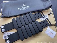 Set of six black Tosamc Sports exercise body weights laid out on boxes with a black carrying pouch in background.