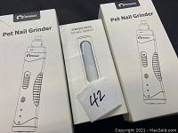 Three boxed Pet East pet nail grinders, white with black details, shown with front packaging and set arrangement.