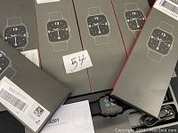 Five black digital smartwatches in branded packaging boxes with watch face design on front. Sticker with number 54 on one pack.