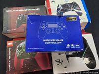 Photo showing the five game controllers, three in boxes and two loose, stacked inside a larger box.