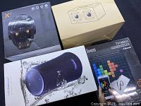 Four boxed Bluetooth speakers and one unboxed wooden dual driver speaker, showing variety in models and designs.