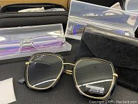 Close-up of black geometric polarized sunglasses with anti-blue ray lenses and a black soft case, along with some translucent and light-colored glasses in cases