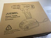 Photo of the box showing JUEMEL 20V Cordless Drill model M8828 packaging with safety warning.