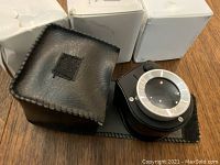 Four Illuminate currency zoom eye pieces each in black and silver with accompanying fabric pouches and original boxes, laid out on wooden surface.