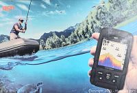 Image of hand holding Luckylaker fish finder showing sonar screen with underwater terrain and fish icons, outdoors with fishing scene background.