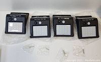Four new solar sensor wall LED lights shown together with mounting hardware in plastic bags.