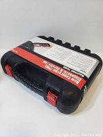 Black hard plastic case with red latches and product info sticker showing the tool and features.