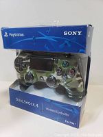 Sony DualShock 4 wireless controller in original blue packaging, displayed at an angle showing controller's camouflage design.