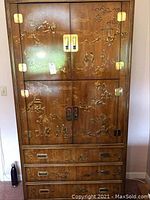 Full front view of tall wooden cabinet with Asian-inspired gold detailing on doors and drawers.