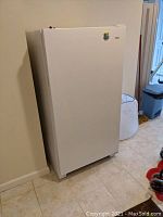 White upright freezer, showing full front and side, positioned in basement.