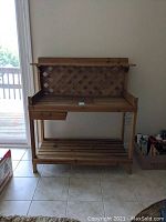 Front view of wooden potting bench showing lattice back, drawer on left, foldable top surface and lower slatted shelf.