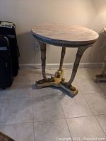 Side view of round marble top on gilded wood base showing pink marble and ornate carved legs.