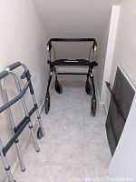 Black four-wheel walker with seat and hand brakes between two walls
