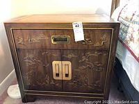 Full view of wooden nightstand side table showing one drawer and cabinet with engraved Asian landscape design and metal handles.
