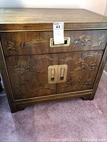 Front view of wooden side table showing Asian-themed carvings and brass handles